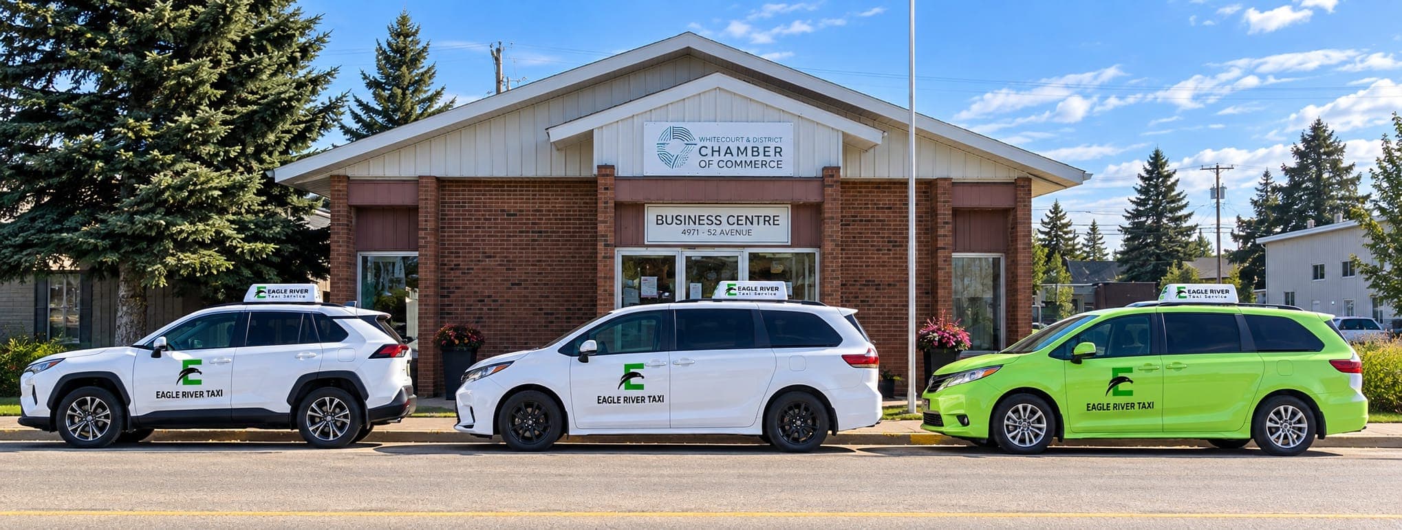 White and green Eagle River Taxi vehicles outside a community building.